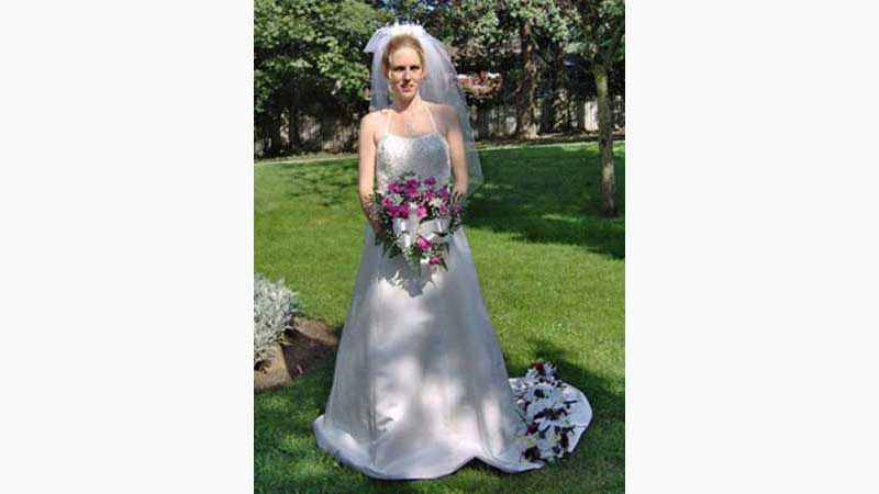 From wedding 2, Hamilton DJ, Beautiful blonde hair bride holding bouquet of flowers and flowers laying on top of her dress which is flowing on to the grass. Sunshine is beautifully highlighting the photo. Taken in Kitchener Ontario